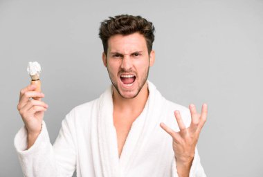 Yakışıklı genç sinirli, sinirli ve sinirli görünüyor. Bornoz giyiyor ve traş oluyor.