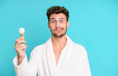 Şaşkın ve kafası karışık görünen yakışıklı bir genç. Bornoz giyiyor ve tıraş oluyor.