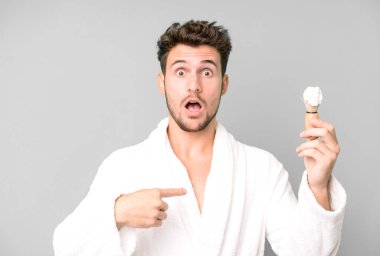 Yakışıklı bir genç ağzı açık, şaşkın ve şaşırmış görünüyor. Bornoz giyiyor ve traş oluyor.