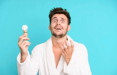 Yakışıklı genç umutsuz görünüyor, sinirli ve stresli bornoz giyiyor ve traş oluyor.