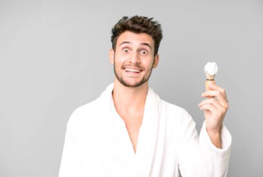 Yakışıklı genç mutlu ve hoş bir şekilde şaşırmış bornoz giyiyor ve traş oluyor.