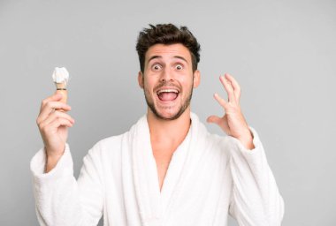 Elleri havada, bornoz giyip, traş olurken çığlıklar atan yakışıklı bir genç.