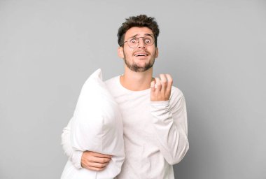 Yakışıklı genç umutsuz görünüyor, sinirli ve stresli pijama ya da gece elbisesi ve yastık giyiyor.
