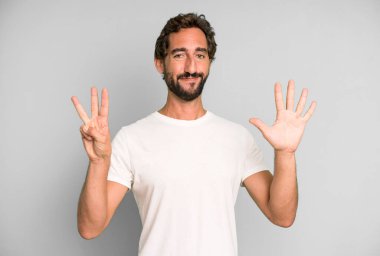 Genç çılgın adam gülümsüyor ve arkadaş canlısı görünüyor, 8 ya da 8 numarayı gösteriyor, elleri önde, geriye doğru sayıyor.