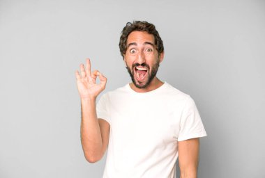 Genç çılgın adam kendini başarılı ve tatmin olmuş hissediyor, ağzı açık gülümsüyor, elle işaret veriyor.