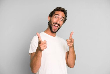 Olumlu, başarılı, mutlu bir tavırla gülümseyen genç çılgın adam kamerayı işaret ediyor, elleriyle silah işareti yapıyor.