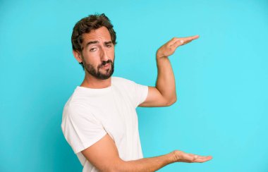 Genç çılgın bir adam iki eliyle fotokopi alanında bir nesneyi tutuyor, bir nesneyi gösteriyor, sunuyor ya da reklamını yapıyor.