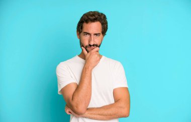 Genç çılgın adam ciddi görünüyor, düşünceli ve güvensiz, bir kolu çapraz ve çene üzerinde, seçenekleri tartıyor