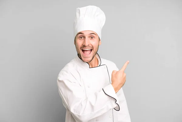 英俊的少年面带微笑地指着侧面 显得兴奋而惊讶 厨师概念 — 图库照片