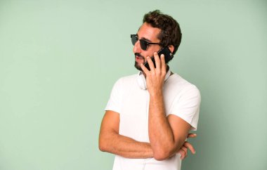 Genç, çılgın, sakallı ve etkileyici bir adam telefonunu kullanıyor.