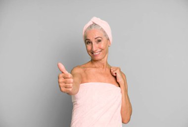 Gri saçlı, güzel bir kadın gururlu, olumlu gülümsüyor. Bornoz ve havlu giyiyor. güzellik konsepti