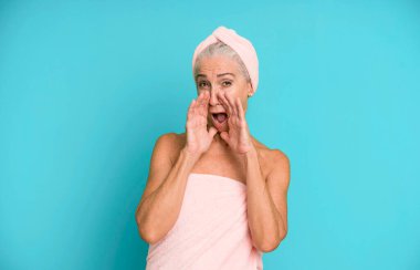Gri saçlı, güzel bir kadın, mutlu hissediyor, elleri ağızının yanında kocaman bağırıyor. Bornoz ve havlu giyiyor. güzellik konsepti