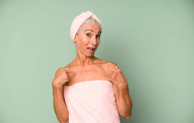 Gri saçlı, güzel bir kadın mutlu hissediyor ve heyecanla kendini işaret ediyor. Bornoz ve havlu giyiyor. güzellik konsepti