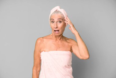 Gri saçlı güzel kadın mutlu, şaşkın ve şaşkın görünüyor. Bornoz ve havlu giyiyor. güzellik konsepti