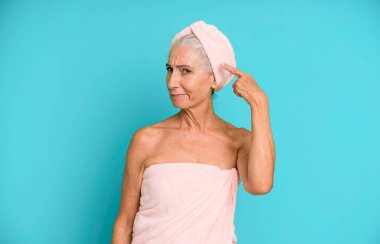 Gri saçlı güzel kadın, kafası karışık ve şaşkın hissediyor, deli olduğunu gösteriyor. Bornoz ve havlu giyiyor. güzellik konsepti