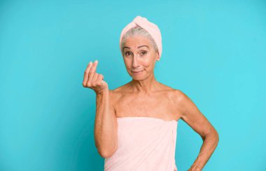 Gri saçlı, güzel bir kadın kapiş ya da para hareketi yapıyor, sana ödemeni söylüyor. Bornoz ve havlu giyiyor. güzellik konsepti