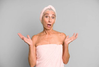 Gri saçlı, güzel bir kadın inanılmaz bir sürprizle şaşkına döndü ve hayrete düştü. Bornoz ve havlu giyiyor. güzellik konsepti