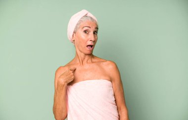 Gri saçlı, güzel, şaşkın ve ağzı açık, kendini işaret eden bir kadın. Bornoz ve havlu giyiyor. güzellik konsepti