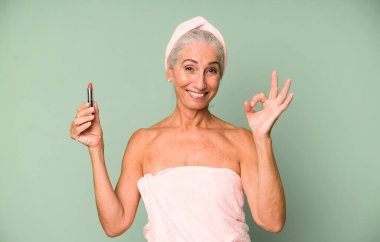 Gri saçlı, son sınıf güzeli, bornoz giyip makyaj yapan güzel bir kadın..