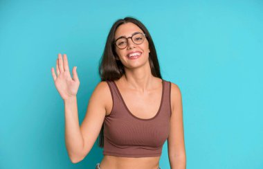 İspanyol güzel kadın mutlu ve neşeyle gülümsüyor, el sallıyor, seni selamlıyor ya da veda ediyor.