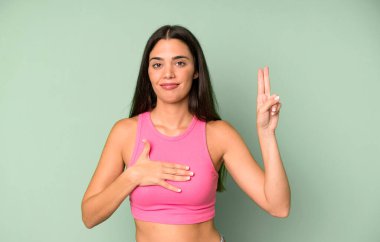 İspanyol güzel kadın mutlu, kendinden emin ve güvenilir görünüyor, gülümsüyor ve zafer işareti gösteriyor, olumlu bir tavırla.