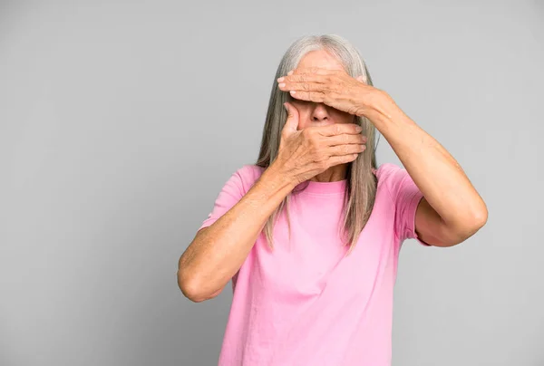 pretty gray hair senior woman covering face with both hands saying no to the camera! refusing pictures or forbidding photos