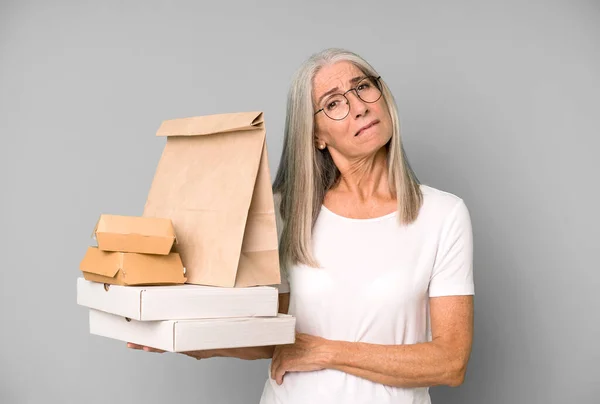 gray hair pretty woman shrugging, feeling confused and uncertain with take away fast food packaging.