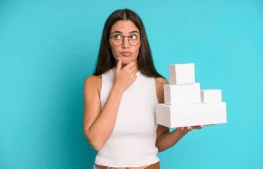 Hispanik güzel kadın düşünüyor, kuşkulu hissediyor ve beyaz boş kutularla karıştırıyor.