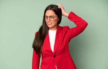 İspanyol güzel kadın şaşkın ve kafası karışmış hissediyor, kırmızı ceketle kafasını kaşıyor. iş kavramı