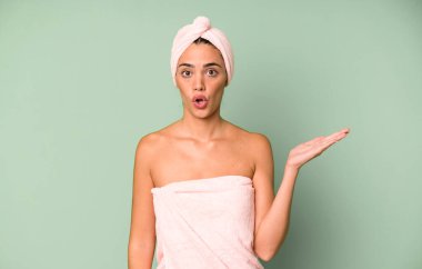 İspanyol güzel kadın şaşırmış ve şok olmuş görünüyor. Çenesi düşmüş ve elinde bir nesne var. Bornoz ve güzellik konsepti