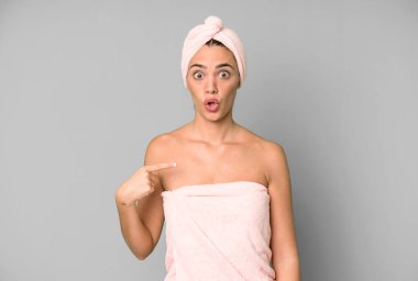 İspanyol güzel kadın şok olmuş ve ağzı açık bir şekilde kendini işaret ederek şaşırmış görünüyor. Bornoz ve güzellik konsepti