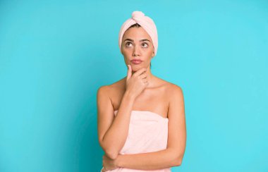 Hispanik güzel kadın düşünüyor, kuşkulu ve şaşkın hissediyor. Bornoz ve güzellik konsepti