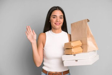 İspanyol güzel kadın mutlu bir şekilde gülümsüyor, el sallıyor, seni selamlıyor ve selamlıyor. boş ambalaj kutularını kaldır