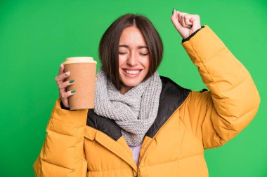 Kışlık kıyafetler giyen ve elinde kahve tutan genç ve güzel bir kadın.