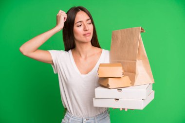 Genç, güzel bir kadın kafası karışmış ve kafası karışmış hissediyor. Kafasını kağıt maketi ile kaşıyor. Fast food ambalajını kaldırıyor.