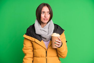 Genç, güzel bir kadın üzgün, üzgün ya da kızgın ve palto giymiş elinde kahveyle yan tarafa bakıyor.