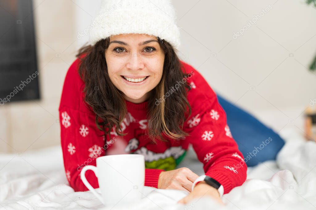 Beautiful brunette in her fourties posing for holiday portrait with a cup of hot beverage in front of a Christmas tree