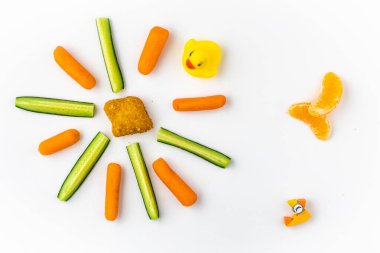 Tavuk nugget, mini havuç, salatalık dilimleri ve oyuncaklar çocuk menüsü olarak dizilmiş.