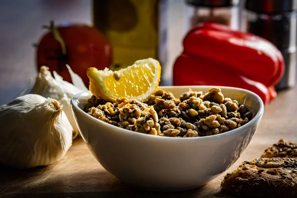 Limon dilimiyle süslenmiş haşlanmış ve baharatlı mercimek ile dolu bir kase. Arka planda çok tahıllı ekmek ve sarımsaklı yonca.