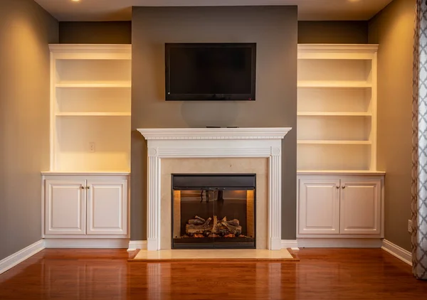 Cabinets on the wall of an empty living room with white shelfs, small tv and fireplace