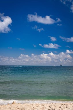 Kumsal, kum, dalgalar ve gökyüzü ufukta bir gemiyle