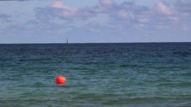 Çekimin sol tarafında parlak turuncu şamandıra yüzüyor. Güney Florida 'daki Fort Lauderdale sahillerine yakın. Hafif güneşli bir günde ufukta görünen bir yelkenli..