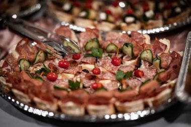 Salam ve kurutulmuş et parçaları, gümüş renkli bir tabakta sergilenmiş vişneli domateslerle süslenmiş bir etkinlik için servis edilmeye hazır.