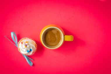 Parlak pembe arka planda duble espresso ile dolu küçük sarı bardak. Açık mavi papyonlu beyaz kremalı kek ve kahvenin yanına renkli şekerlemeler..