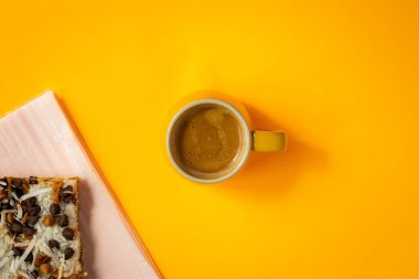 Sarı duble espresso kahve fincanı, açık sarı arka planda. Hindistan cevizi hapları ve çikolata parçacıklarıyla süslenmiş katmanlı hamur işi..