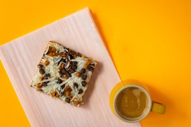 Sarı arka planda bir fincan espresso. Hindistan cevizi parçalarıyla kaplı çok katmanlı pasta diliminin yanında.