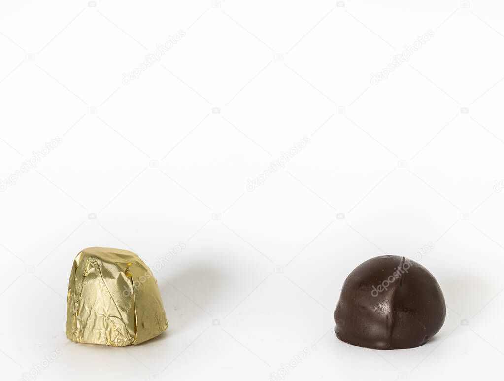 Two candies on white background. One is wrapped in gold coated foil, the other is just bare dark chocolate.