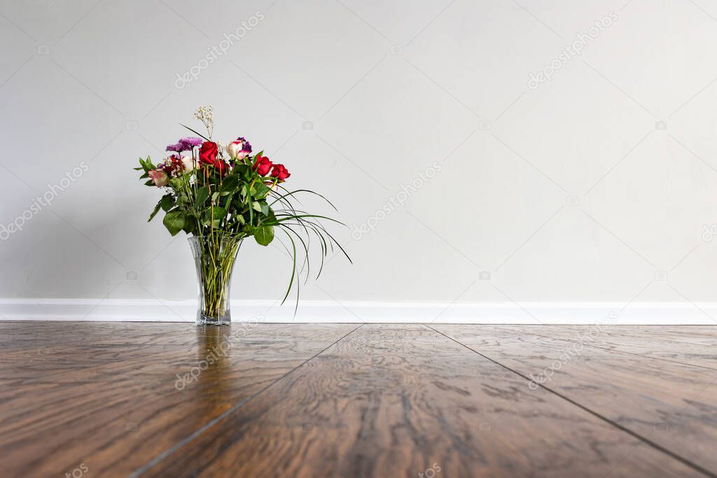 Flower arrangement on hardwood floor of an empty room with white wall