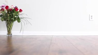Vase with roses placed on the floor of a room with white wall