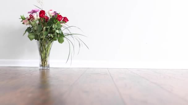 白い壁を持つ空の部屋の堅木張りの床に置かれた花の配置の前に右から左へスライド — ストック動画